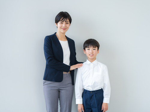 スーツの女性が子供の肩に手をかけて共に将来を考えている写真