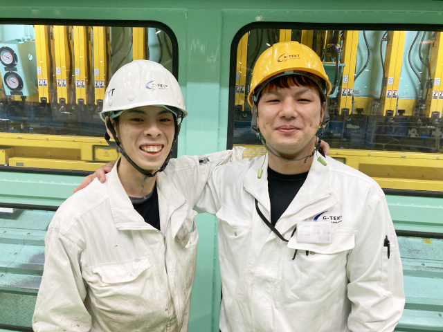 ジーテクト群馬工場内、作業服を着た男性2人が肩を組んでいる写真