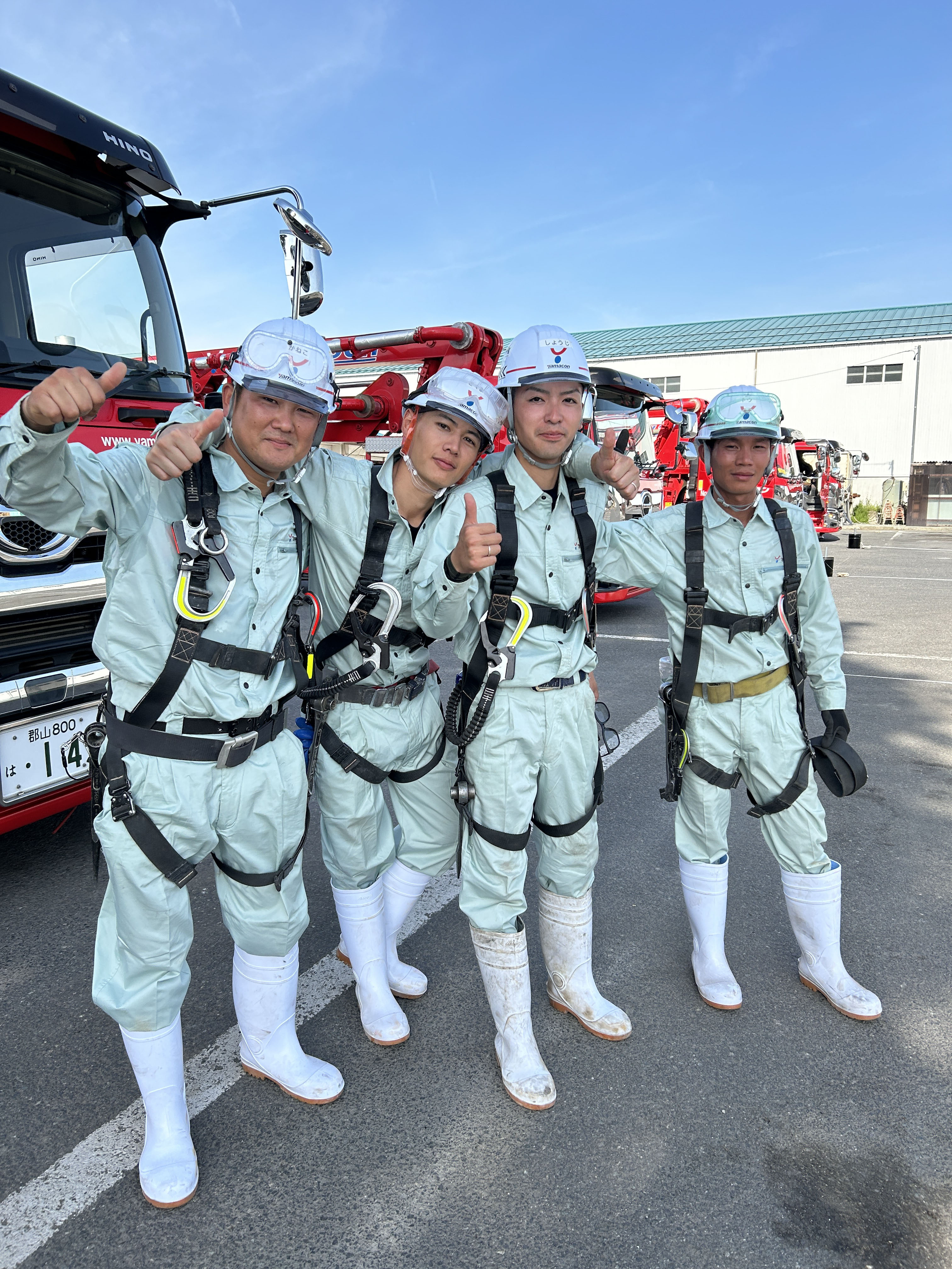 屋外でヘルメットとフルハーネスを装着した男性4名が並んでいる写真