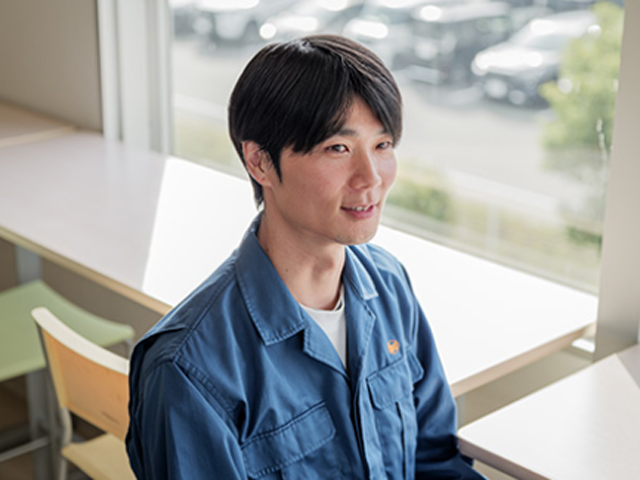 細川洋行　椅子に座ってインタビューを受ける青い作業服の男性