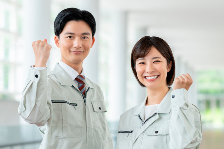 笑顔でガッツポーズをする作業服の男女スタッフ