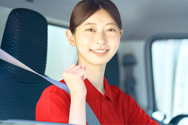 トラックの運転席に座る赤いポロシャツを着た女性の写真