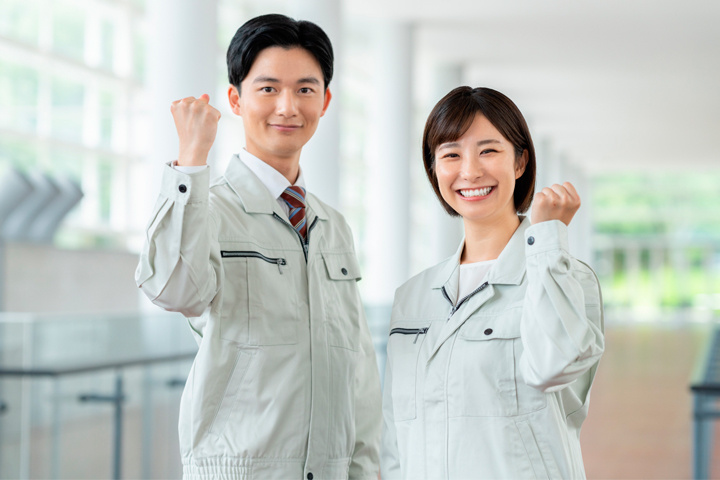 笑顔でガッツポーズをする作業服姿の男女の写真