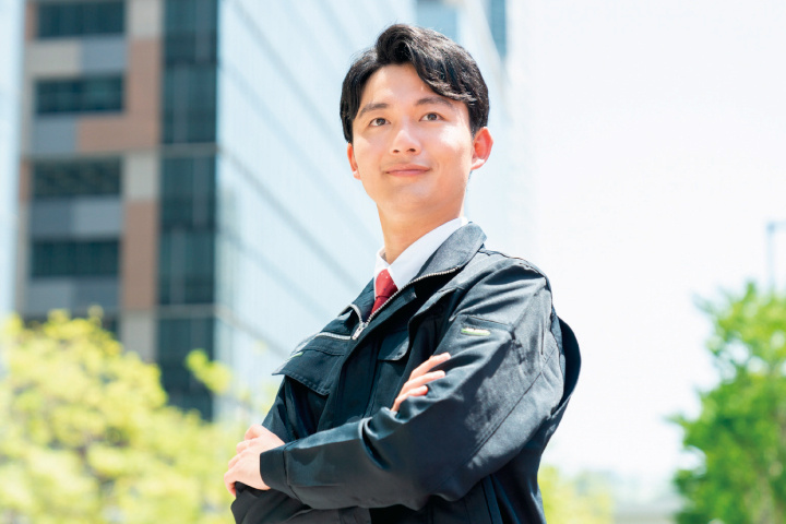 腕組みをして微笑む作業服姿の男性の写真