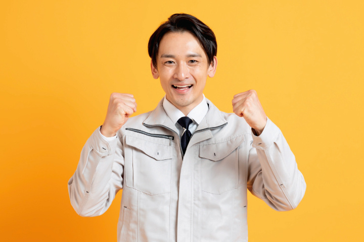 両手でガッツポーズをする作業服姿の男性の写真