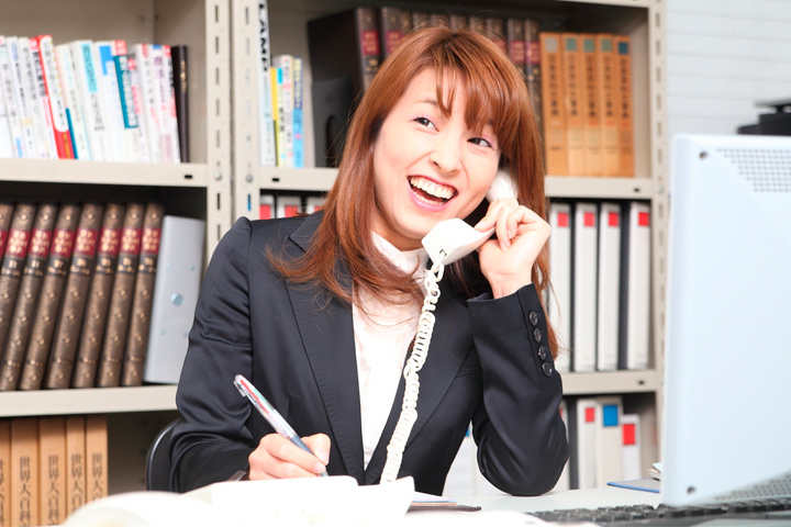 電話をしながらメモを取る女性事務スタッフ