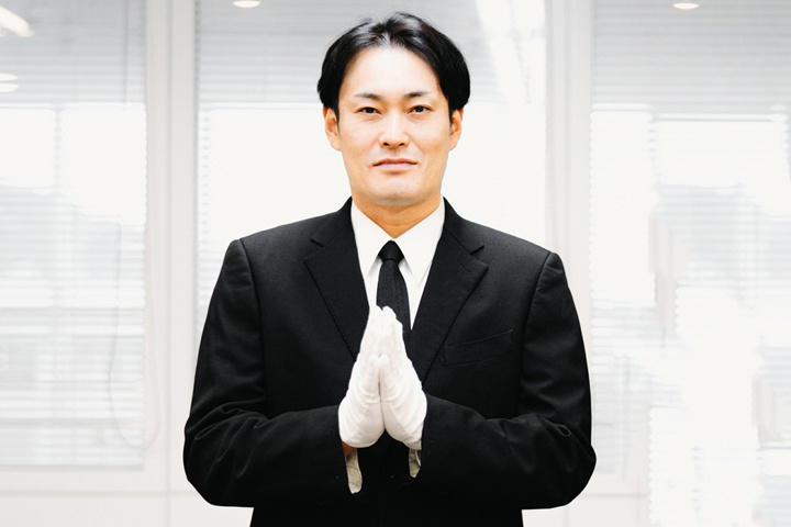 合掌する白手袋をつけた礼服姿の人物写真