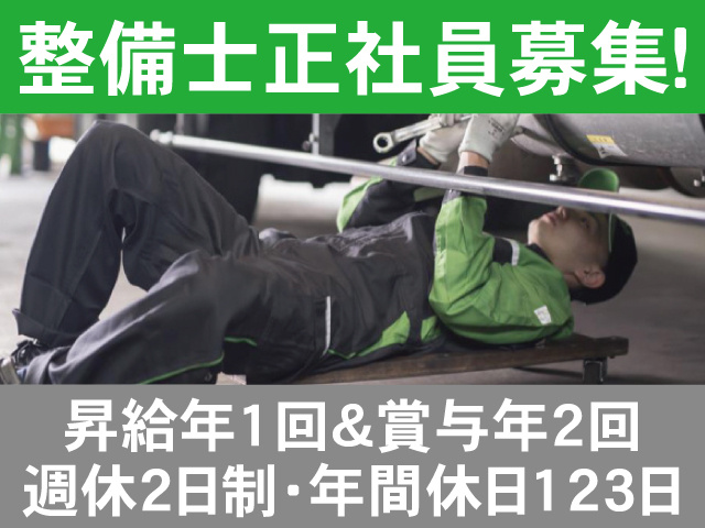 整備士正社員募集！昇給年1回＆賞与年2回。週休2日制・年間休日123日。車体の下に仰向けで潜り、整備している男性の写真。