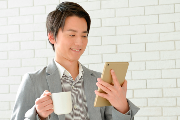 コーヒーを飲みながらタブレットを見ているスタッフ写真