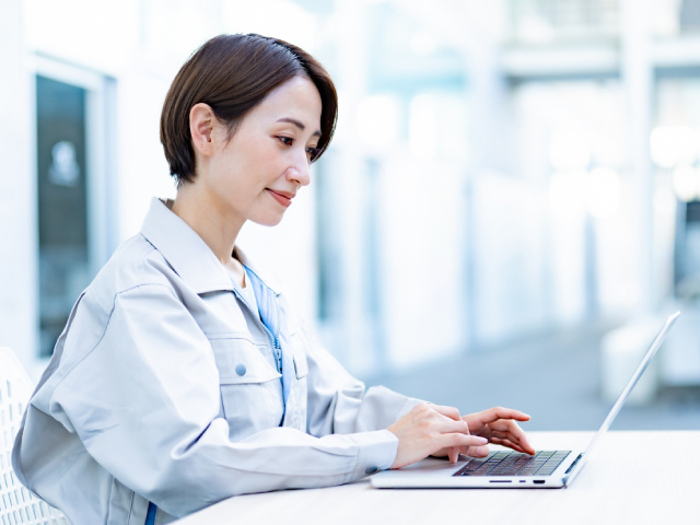 作業着を着た女性がパソコン操作をしている写真