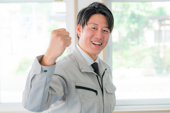 作業着を着用した男性社員がガッツポーズをしている写真